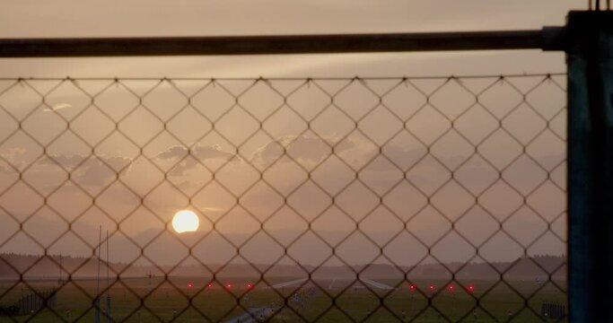 Sunset behind Ljubljana airport fence in Slovenia. Big sun is setting behind the Alps. View of empty runway. Colorful summer evening. Real time static shot