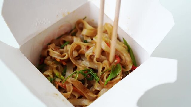 Delivery of ready-made Asian food. noodles with vegetables and seafood in a white box and sushi sticks. Delicious dinner. order food over the phone or online. 