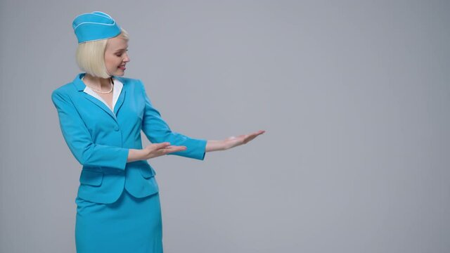 Attractive smiling blonde stewardess points to an empty space. Gray background.
