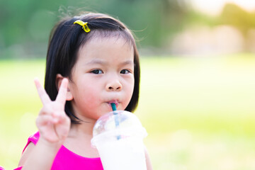 Asian girl sucks fresh coconut milk from a plastic cup to cool off. On a hot day. Cute child held...