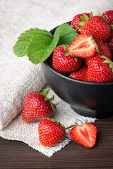Close-up photo of strawberry in black bowl with a green leaf near white towel on a dark table. Strawberry concept