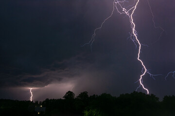 Night photo of two lightnings in the sky over a small village. One lightning close to the viewer, the other one smaller in the background