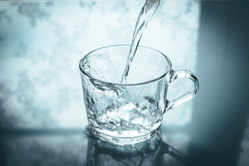 Pouring water into a glass, blue pastel background