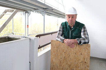 funny elderly builder with building materials in a white helmet protection and working uniform works at a construction site for the construction and repair of buildings