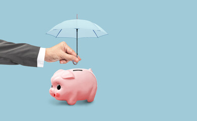 Protect your investment for future fund concept, Hand holding light blue umbrella over piggy bank...
