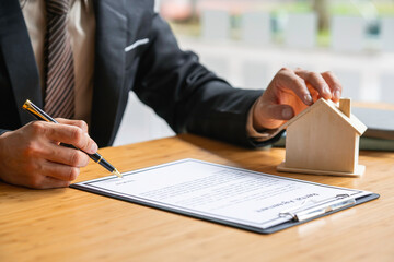 Real estate agent holding home and signing a contract about the agreement of real property on desk, businessman writing on document form rent house, broker and planning investment, business concept.