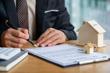 Real estate agent holding home and signing a contract about the agreement of real property on desk, businessman writing on document form rent house, broker and planning investment, business concept.