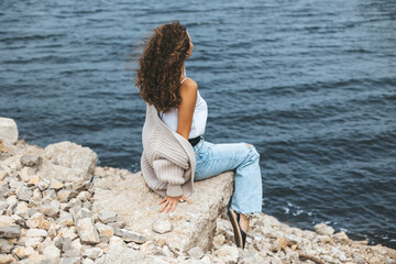 Young woman from behind sitting on rocky river bank