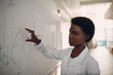 African American woman math teacher writing on blackboard with marker. - obrazy, fototapety, plakaty
