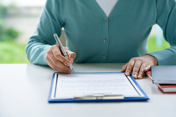 Businesswoman signing a document or application form in a folder, Woman signing document with pen on a desk at home
