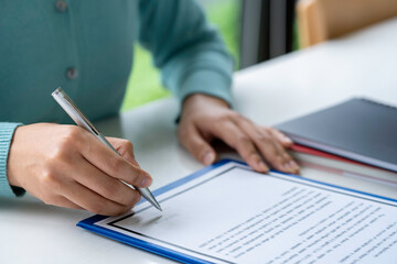 Businesswoman signing a document or application form in a folder, Woman signing document with pen on a desk at home