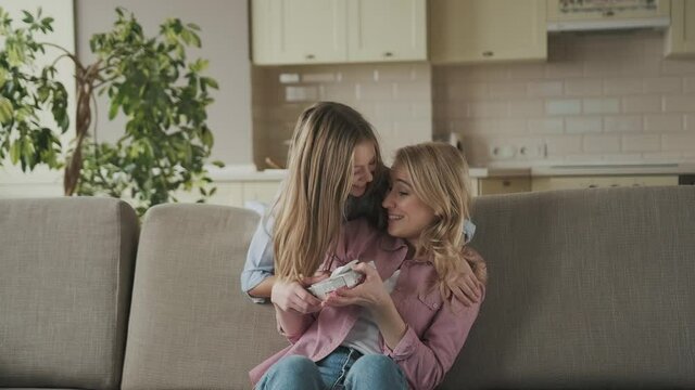 Happy women's day. Child daughter is congratulating mom and giving her postcard and gift. Mum and girl smiling and hugging. Family holiday and togetherness.