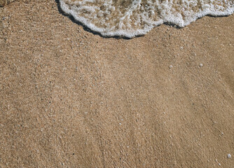 A sea wave with foam rolls over the sand, top view. Copy space.