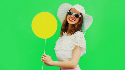 Summer portrait of cheerful happy smiling young woman with yellow balloon wearing a white straw hat on green background