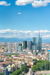 Obraz premium Vertical aerial view of Milan skyline, Italy, with business skyscrapers. In the distance the alps mountain range is visible. Blue sky and white clouds on the background.