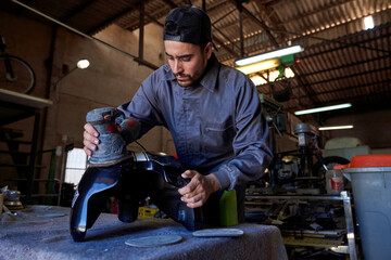Male mechanic polishing metal detail with orbital sander