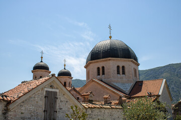 Fototapeta na wymiar Church towers visible against the backdrop of a mountain landscape and green trees and sky. Old medieval church in backdrop of the mountains in Kotor Montenegro