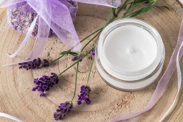 Obraz na płótnie Canvas Cream jar with lavender extract or essential oil, sachet of dried flowers and fresh lavender on wooden board. Top view. Aromatherapy or wellness or skin care concept