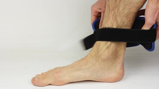 Man Removes Ankle Weights From Leg On White Background, Sport Or Fitness Equipment For Workout Or Fitness Training