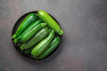 Zucchini in a black plate on a gray-brown background. Top view, copy space.
