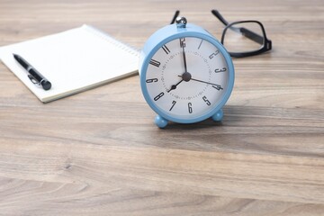 Selective focus on the alarm clock with a pen on the notebook and eyeglasses at the back