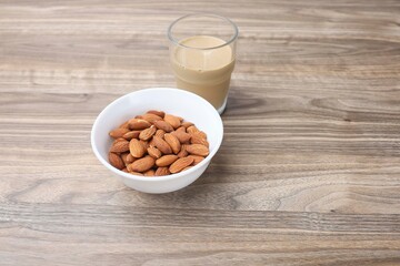 A bowl of almond nut and a glass on coffee on the wooden table 