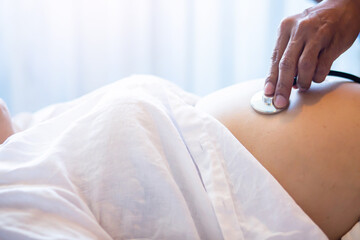 Doctor using stethoscope examining pregnant woman in clinic. 
 Medical exam concept. Young preganant woman expecting a baby doctor visit. Healthcare and medical concept.