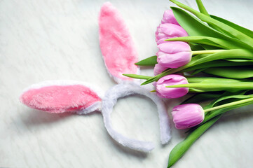 Easter composition or postcard. Bouquet of purple tulips and decorative fluffy rabbit or hare ears on a white marble background, top view.
