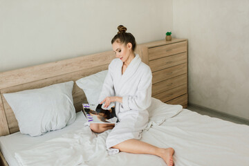 Woman in white robe stay near the window and on bed in hotel room