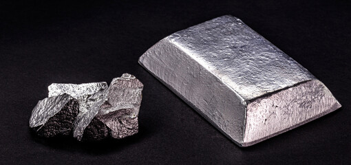 Insulated zinc ingot or bar next to raw zinc nugget on insulated black background, metal used in...
