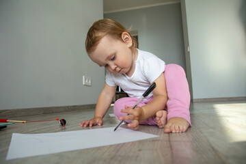 Little cute girl draws on white paper on the floor