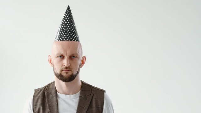 Birthday alone. Boring party. Holiday melancholy. Sad unhappy disappointed bald man wearing cone hat isolated on light neutral copy space background.