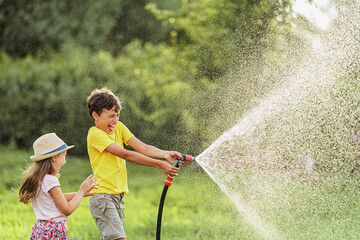 happy kigs splashes and plays with garden hose with sprinkler at sunset in backyard, enjoys...