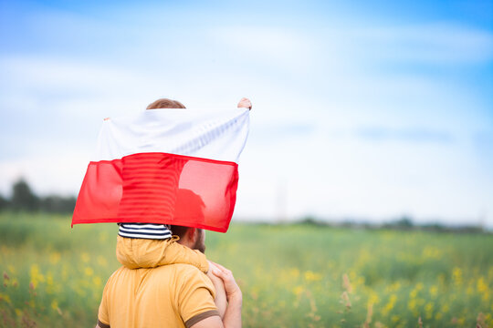 Dad with his little son on his shoulders walking in the field holding flag of Poland. Father's day in Poland. Polish Flag Day. Independence Day. Love Poland, travel concept. Selective focus. - Powered by Adobe