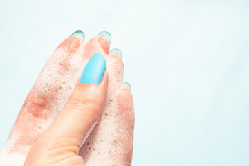 female fingers in white soapy foam on a blue background