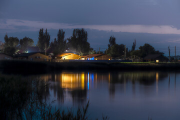 Obraz premium Landscape of the night city on the water, the reflection of lonely glowing houses in the water.
