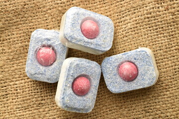 Four dishwasher tablets on burlap, close-up, top view.