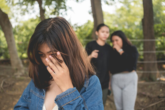 A young woman sobs aware of two women making fun of her and spreading false gossip. Bullying in female teens.