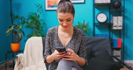 Portrait of a Beautiful Caucasian Teenage Girl in Cozy Living Room Using Smartphone at Home. She's Browsing the Internet and Checking Videos on Social Networks and Typing message.