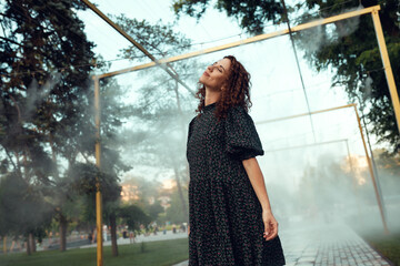 cute red-haired curly girl rejoices under the water fogger in the city center