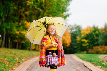 Smiling little girl with umbrella in raincoat and boots outdoor