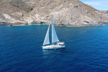 Sailing boat with open white sails, blue sky and rippled sea background