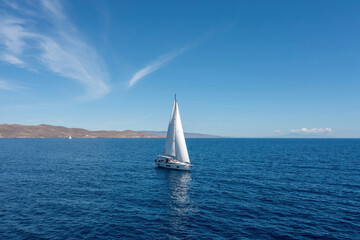 Fototapeta na wymiar Sailing boat with open white sails, blue sky and rippled sea background