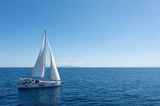 Sailing boat with open white sails, blue sky and rippled sea background