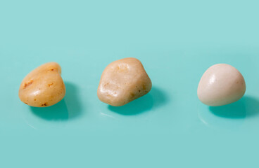 3 small brown stones, similar to pebbles, horizontally lie on a turquoise background.