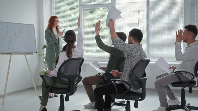 young business woman makes a presentation of new project on flipchart for female and male employees, young man raises his hands and asks for questions during a business meeting in office