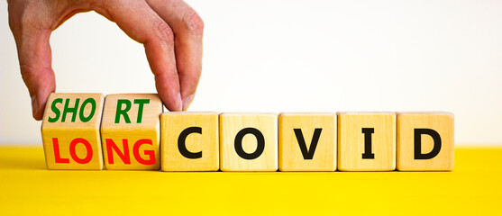 Long covid symbol. Doctor turnes wooden cubes and changes words ' long covid' to 'short covid'. Beautiful yellow table, white background, copy space. Medical, covid-19 pandemic long covid concept.