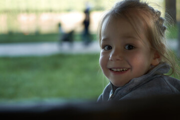 Little happy child girl sitting on a bench having fun in the park