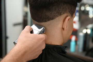 Professional barber making stylish haircut in salon, closeup