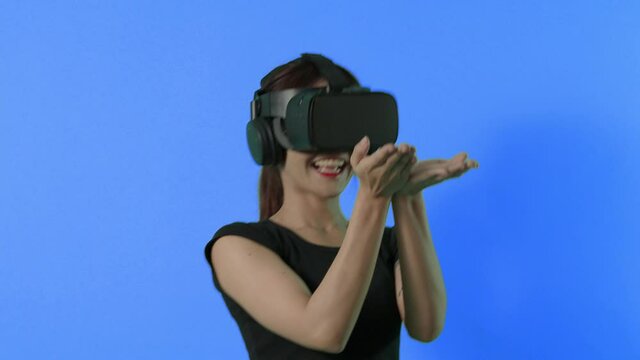 VR game playing. Asian teenager woman playing virtual reality game by VR headset. Blue or green screen background for chroma key. Playing game with happiness and excited. Cyber gaming World. 